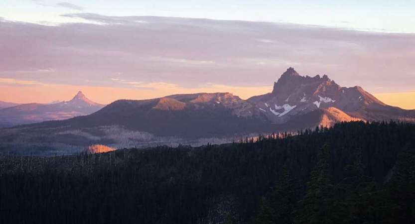 A mountainous landscape appears purple and pink while the sun is either setting or rising. 